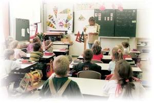 Kinder sitzen im Klassenzimmer und hören ihrer Lehrerin an der Tafel zu.