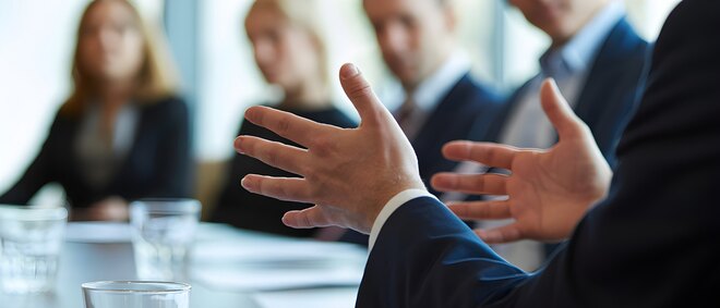 Business leader gesturing during boardroom coaching session with executive team around table, symbolizing leadership development and strategic guidance