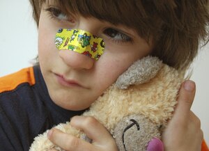 Trauriger Junge mit Pflaster auf der Nase und Stofftier im Arm