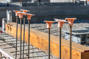 Baustelle mit orangefarbenen Bewehrungskappen auf Stahlbewehrungsstutzen in einer Stahlbetonwand, Fundament zum Schutz der Bauarbeiter und der Baumaterialien