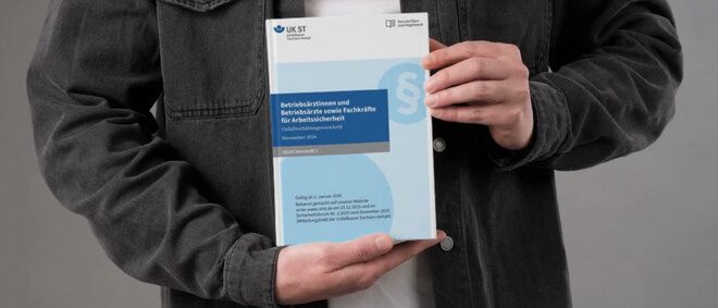 Mann hält Broschüre der DGUV Vorschrift 2 in beiden Händen