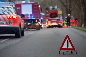 Warndreieck steht geöffnet vor einem Unfallort auf der Straße, hinten Notarzt, Feuerwehr an Unfallstelle