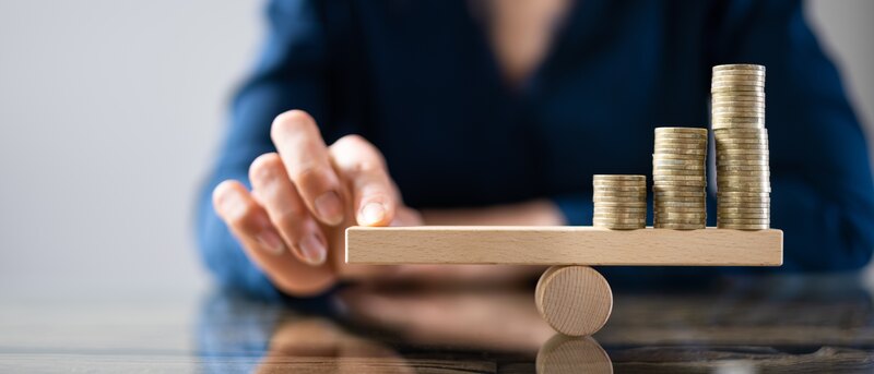 Businessperson Balancing Stacked Coins On Seesaw