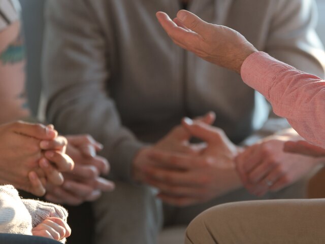 Close-up of a therapist gesticulating while talking to a group of listing teenagers during an educational self-acceptance and motivation meeting.