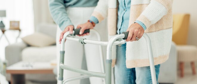 Nahaufnahme einer Pflegekraft, die eine Patientin mit Rollator im Haus begleitet und ihr hilft