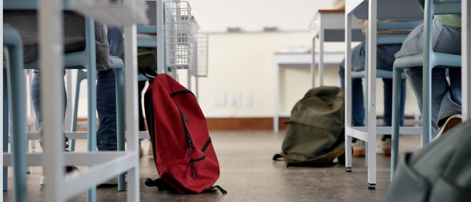 Zwei Rucksäcke liegen auf dem Boden eines Klassenzimmers neben Schülertischen
