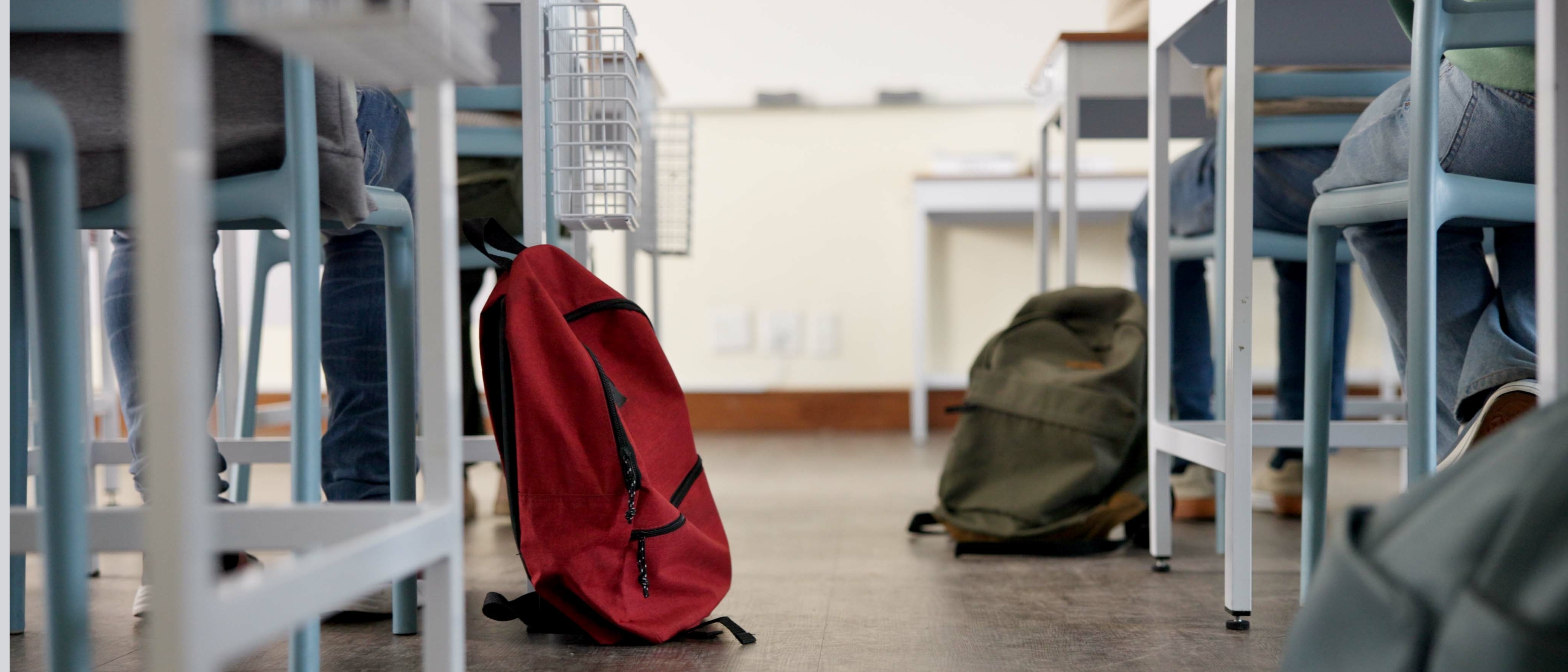 Classroom, backpack and education in school, students and low angle of learning of kids in academy. Desk, legs and children with scholarship, studying and writing of practice exam, bag and knowledge