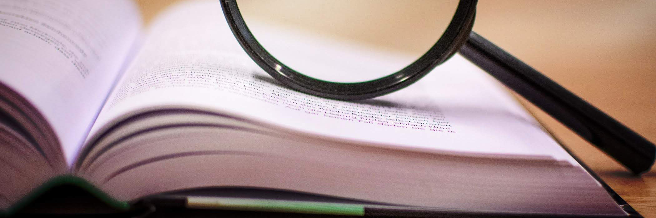 aufgeschlagenes Buch, auf dem eine Lupe liegt